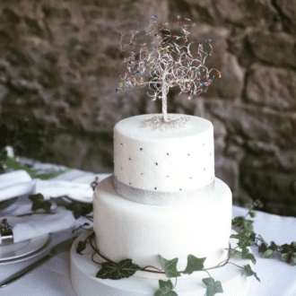 Silver wire wedding tree cake topper decorated with rainbow mix of crystals on the branches sitting on top of a two tiered wedding cake.