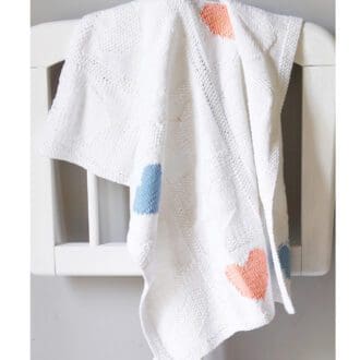 white cotton hand knitted baby blanket decorated with heart motifs
