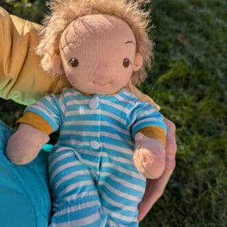 Handmade fabric baby boy doll in a onesie outdoors held in a woman's arms