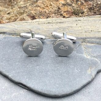 Round silver cufflinks, one featuring a dog and the other featuring a bone.