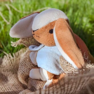 Handmade velveteen bunny with caramel and cream fur and a light blue cloak sitting on sacking with a grass background