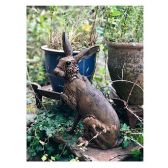 Large sitting Hare Sculpture with a rust finish in a garden setting