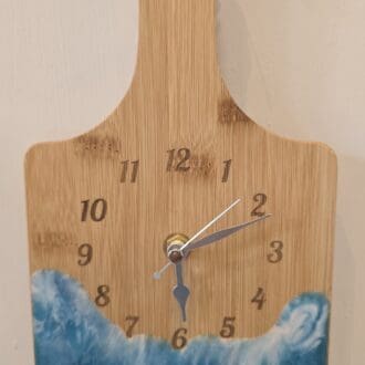 Bamboo chopping board wall clock with engraved numbers and silver hands, featuring a resin wave design in deep blue and white tones.