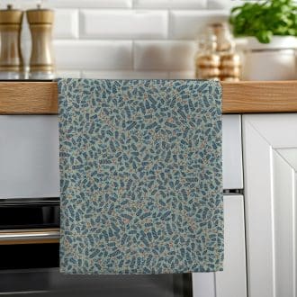 A soft green cotton tea towel featuring a hand-illustrated botanical berries pattern hanging neatly on a wooden oven rail in a bright kitchen.