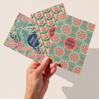 A hand holding three hand-illustrated floral birthday cards featuring The Illustrarium’s original designs: Daisy, Daisy Stripe, and Chinoiserie, each with ‘Happy Birthday’ in the centre and intricate patterned borders.