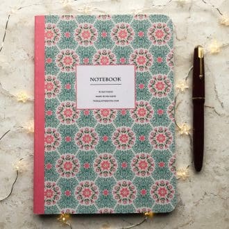 A hand-painted A5 notebook with a pink and green daisy floral pattern, styled with a red fountain pen and soft fairy lights on a marble background.