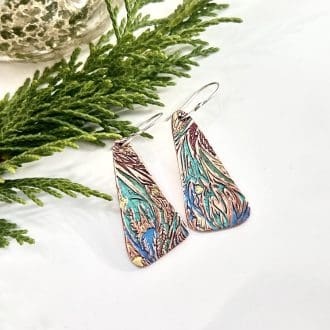 A pair of copper handcrafted drop earrings, long and textured in a swirl pattern and painted in blue, green and plum metallic colours. They have sterling silver ear wires and displayed on a white background.