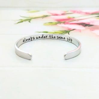 A hand-stamped 6mm aluminium bracelet with the wording always under the same sky hidden inside