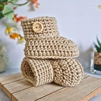 crochet baby booties with Born in 2026 wooden button in colour parchment on a wooden tray. Newborn baby keepsake gift.