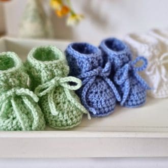 Several pairs of handmade crochet baby booties in white, tea Green and periwinkle blue with a soft textured cuff and seamless finish.