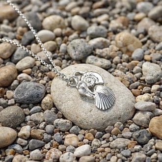 A handcrafted fine silver sea shell necklace, 3 shells joined togther on a sterling silver chain. It is displayed on a stone surrounded by pebbles.