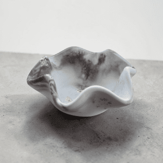 A small dish with wavy edges sits on a black and white marble counter in front of a plain white wall. The dish is black and white marble in colour.