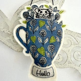 Textile wall hanging of free motion mouse in a blue floral mug with hello message, whimsical decor