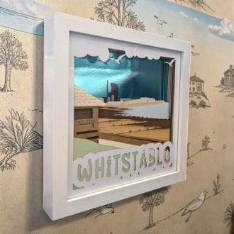 A layered paper art of Whitstable in Kent, as seen from the Bubble café towards the oyster fishery. It is seen from its left edge and is in a white box frame